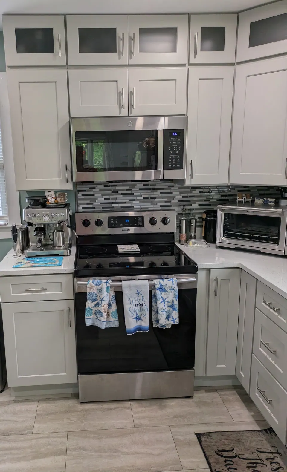 White shaker kitchen with frosted glass cabinets on top, a stainless range and an over-the-range microwave.