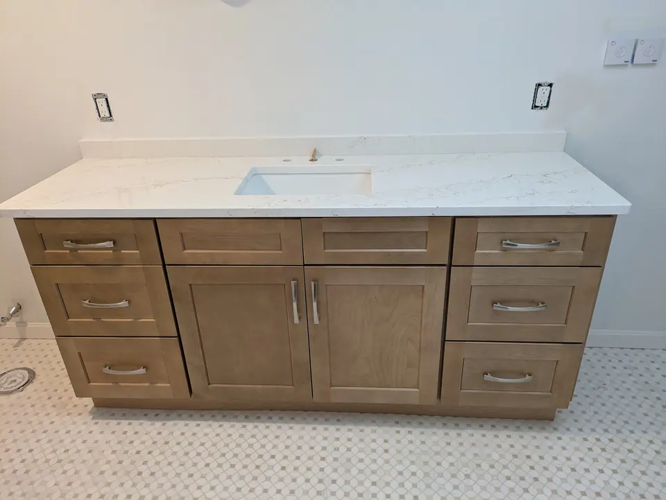 Finished natural wood shaker vanity with drawer stacks on both sides and a white veined top.