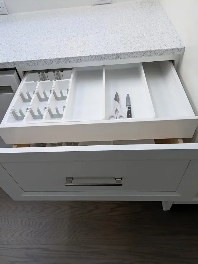 Open white drawer with a sliding upper tray divided for knives and cutlery.