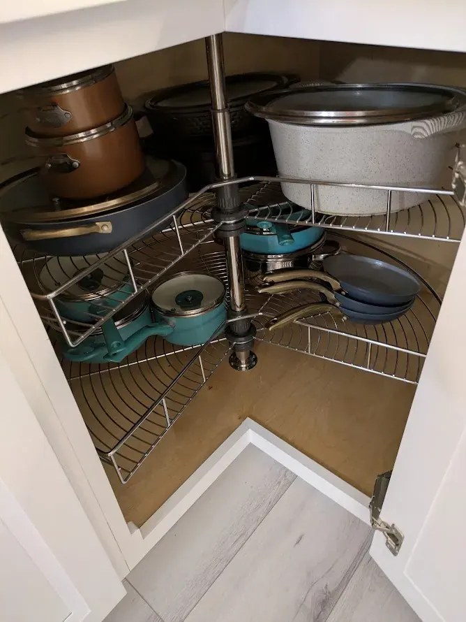 Corner base cabinet open to show a two-tier wire lazy Susan holding pots and pans.