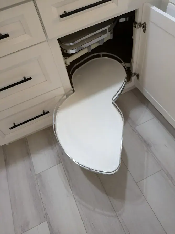 Blind-corner pull-out shelf swung out of the white base cabinet over the gray plank floor.